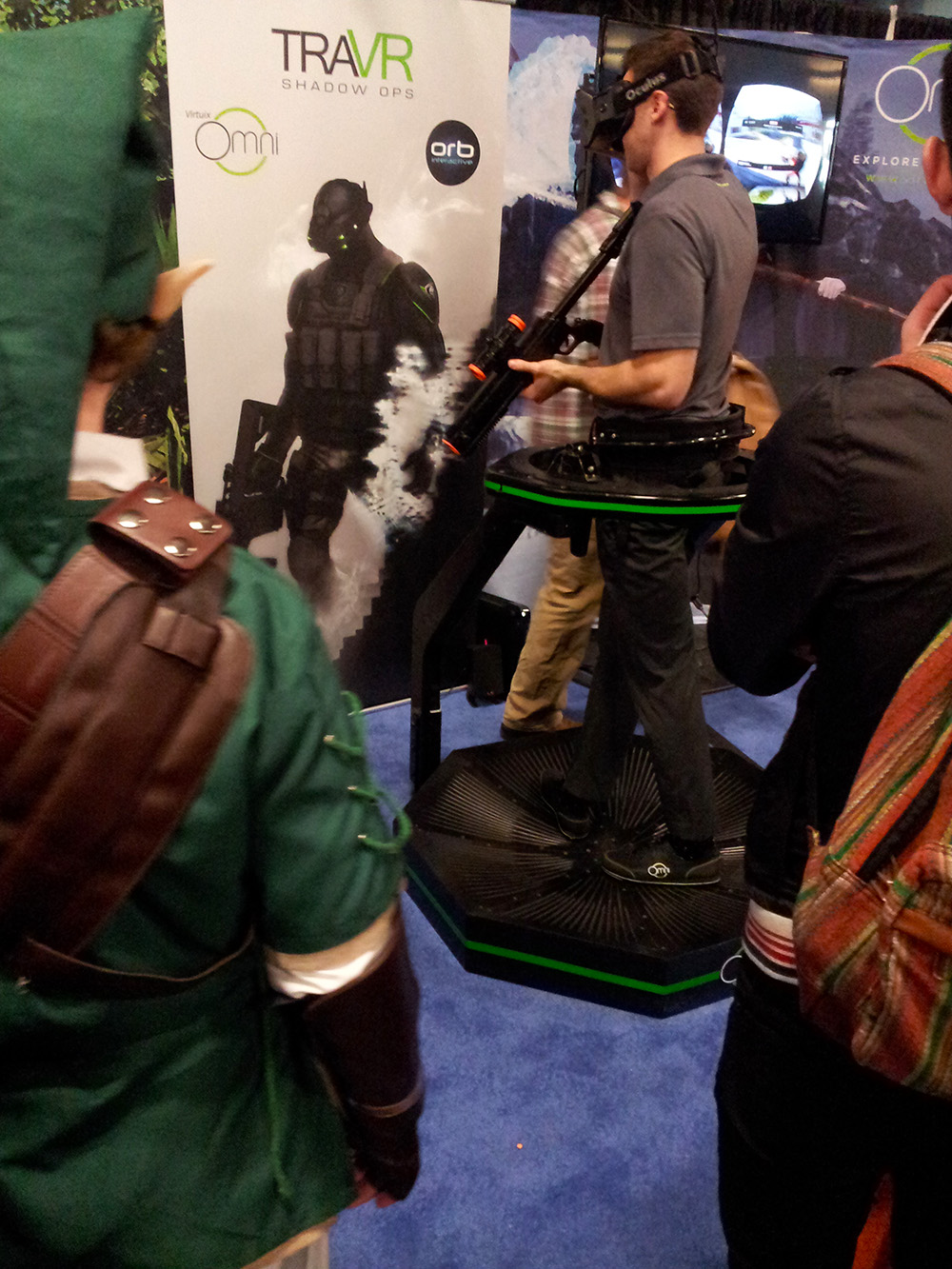 A kid wearing a Link costume from Legend of Zelda looks on while someone wearing an Oculus Rift plays TraVR Shadow Ops.