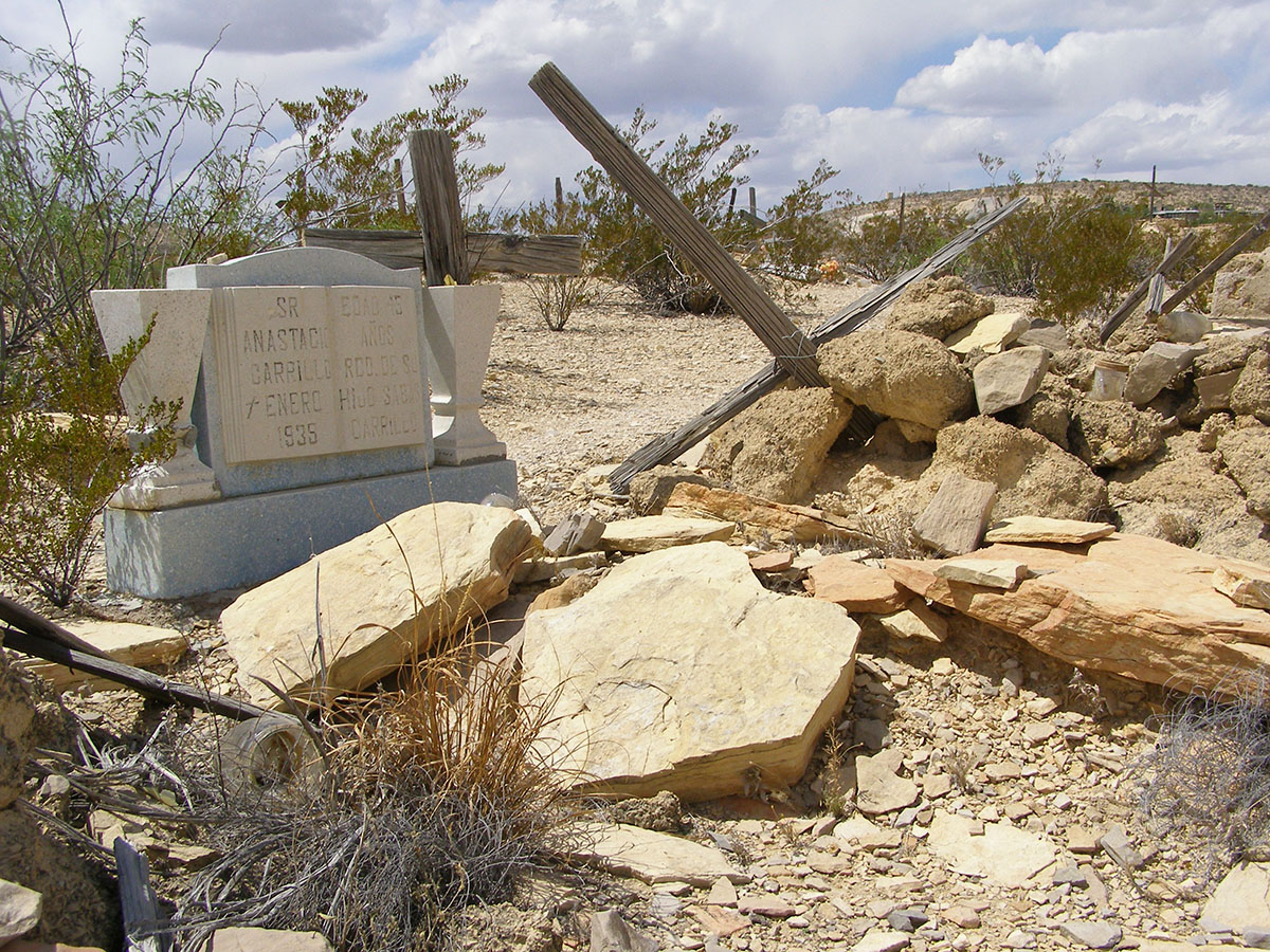 A fallen over cross near a rare conventional headstone.