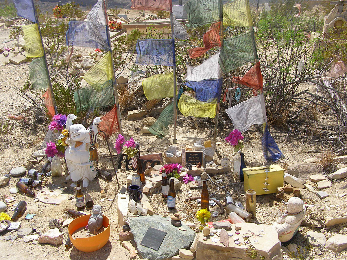 A memorial site with prayer flags and a laughing Buddha statue.