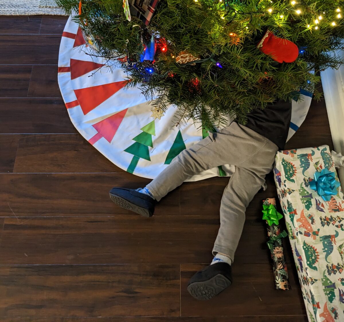 A toddler under a Christmas tree with a colorful tree skirt from Target.